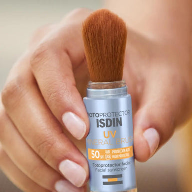 Mano sosteniendo la brocha ISDIN UV Mineral Brush SPF 50 con el protector retirado