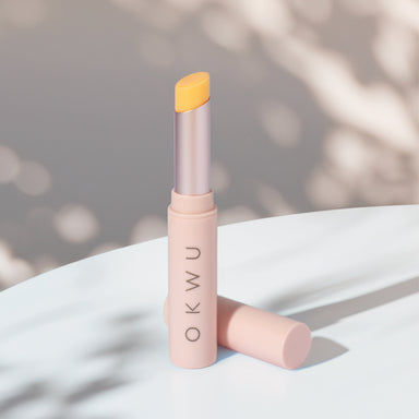 Labial OKWU Magic Lipstick abierto sobre una mesa, barra amarilla y envase rosa pastel con luz natural